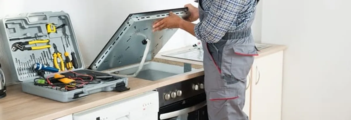Cooktop repair technician lifting a built-in stovetop for service in Jersey City, NJ