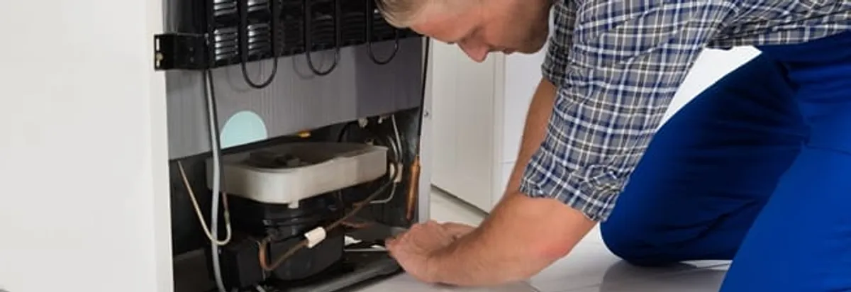 Refrigerator repair technician servicing the compressor and condenser area in Jersey City, NJ
